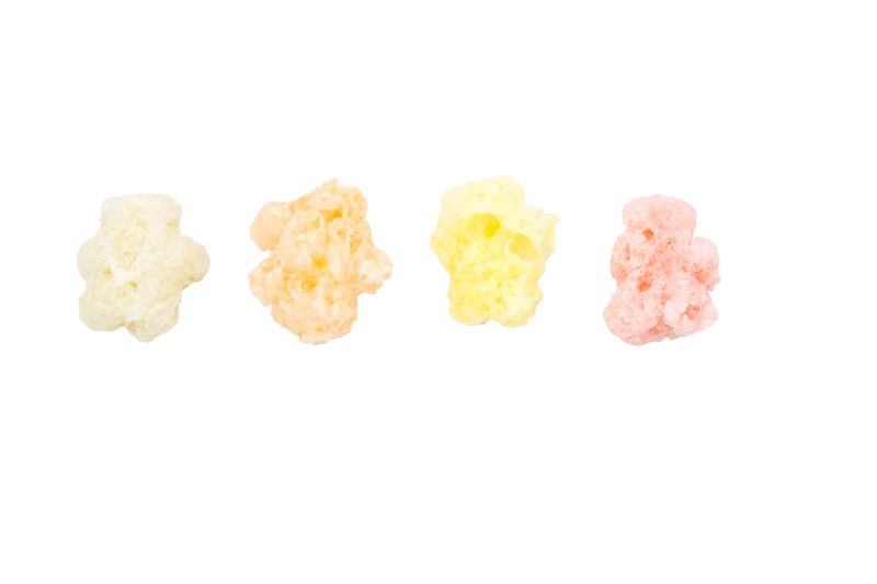 Four pieces of colorful popcorn against a black background, arranged in a row from left to right: white, orange, yellow, and pink—like a vibrant lineup of Sow Good Inc’s Freeze Dried Gummy Bears.