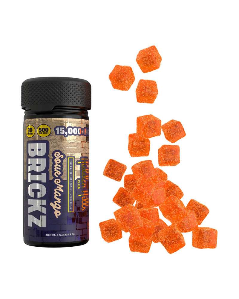 A black bottle labeled "Hidden Hills Heady Blend Brickz Gummies" stands next to a pile of orange gummy candies. The label highlights the inclusion of Delta-8 THC, live resin, and boasts an impressive 15,000mg per container.