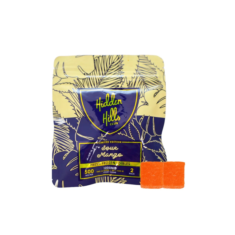 A packet of Hidden Hills edibles labeled "Limited Edition Sour Mango" with two orange Hidden Hills Heady Blend Gummies | 2ct in front. The packet displays information: 1000mg high-quality cannabis extracts, 2 doses of 500mg each.